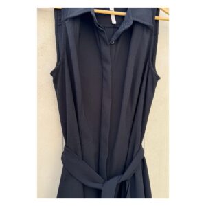 Vestido camisero negro sin mangas Laundry by Shelli Segal con cinturón, modelo de pie descalza sobre fondo cálido tipo chukum, estilo parisino de lujo relajado