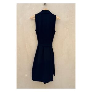 Vestido camisero negro sin mangas Laundry by Shelli Segal con cinturón, modelo de pie descalza sobre fondo cálido tipo chukum, estilo parisino de lujo relajado
